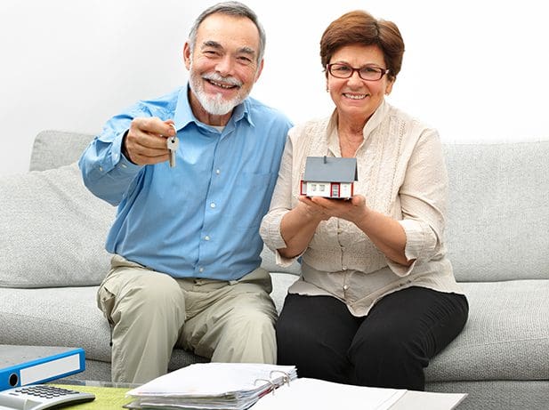 Senior couple holding house keys and model home.