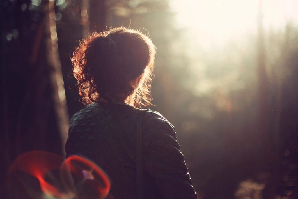 A woman standing in the woods with her back turned.