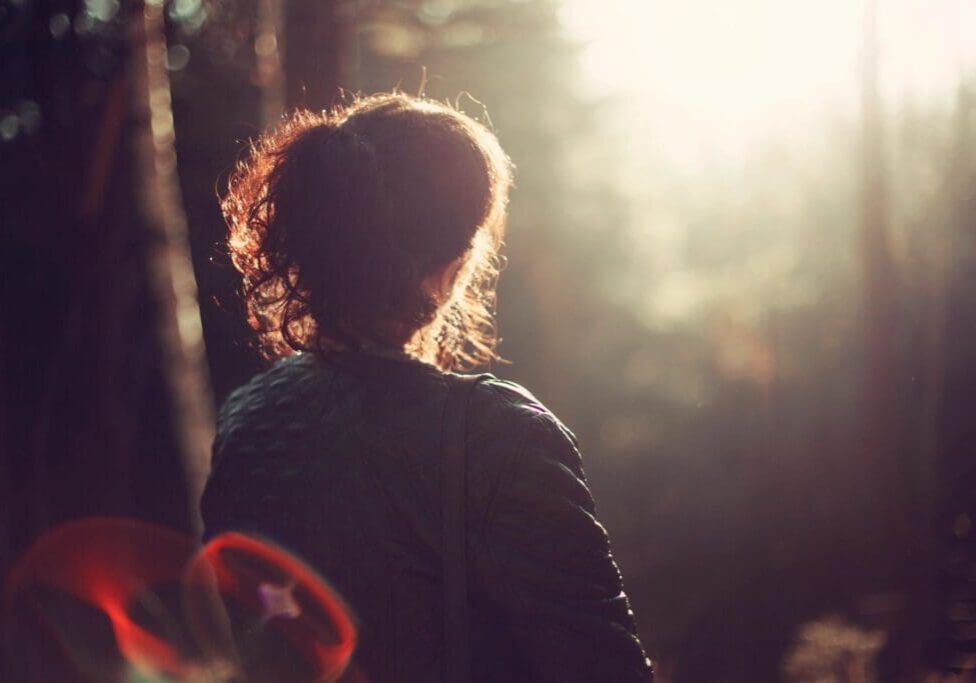 A woman standing in the woods with her back turned.